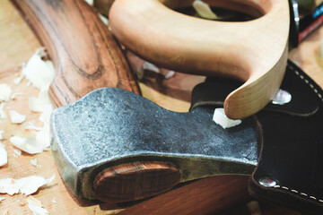 A large, sharp axe with a wooden handle in a leather sheath lies on a wooden table. The handle is skillfully carved and has a natural, rustic look. table is made of wood and has a few small scratches.