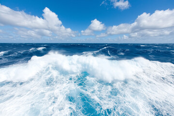 Obraz premium Powerful ocean waves crash under a bright blue sky with scattered clouds, capturing the energy and vastness of the sea