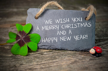 Black slate plate with four leaf clover and with the german words for Merry Christmas and happy new...
