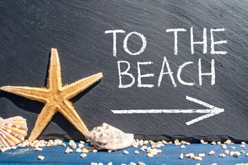 Black slate chalkboard with starfish and sea shells showing the words to the beach