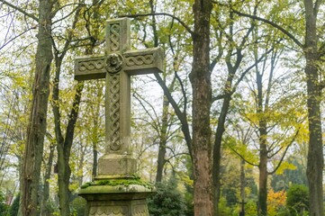 Stone cross standing in a cemetery surrounded by trees in autumn