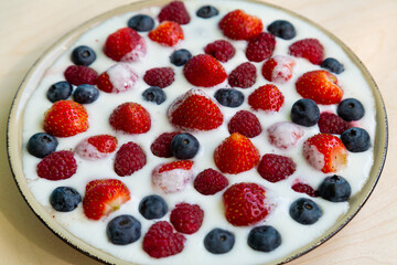 In a plate with freshly whipped cream juicy berries strawberries raspberries and blueberries on a light table