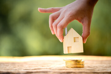 Man hand hold for select the home model put on the wood on sunlight, in the public park, Loan for real estate or saving money for buy a new house to family in the future concept.