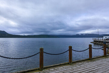 Obraz premium A peaceful view from a wooden pier overlooking a calm bay or lake, with distant mountains lining the horizon. Ideal for scenes of nature, relaxation, and scenic beauty
