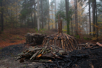 Charcoal pile burning in misty forest setting with stacked firewood
