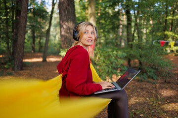 Woman with headphones sitting on a hammock with a laptop in nature