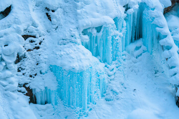 Blue colored icicles from a snowed over frozen waterfall in a canyon on a mountain