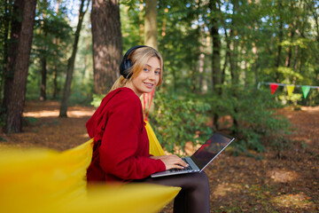 Woman with headphones sitting on a hammock with a laptop in nature