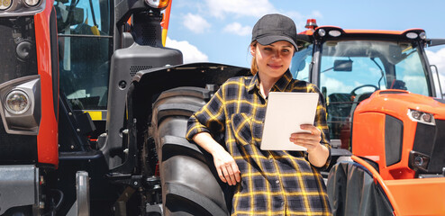 Female farm worker with digital tablet beside tractor at agricultural equipment dealership,...