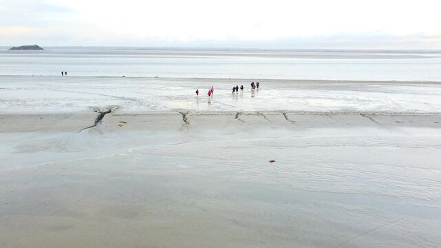 Aerial shot capturing visitors walking on the tidal flats surrounding Mont Saint-Michel, showcasing its breathtaking landscape and historic charm.