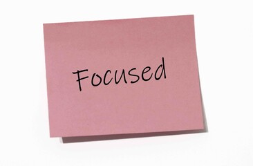 Pink Sticky Note with the Word "Focused" Written in Black Handwriting on a White Background