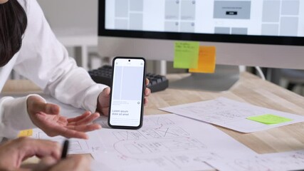UX UI designer testing prototype on a phone, discussing and brainstorming on wireframes for a website and mobile app prototype, in the concept of website and mobile application design concept.