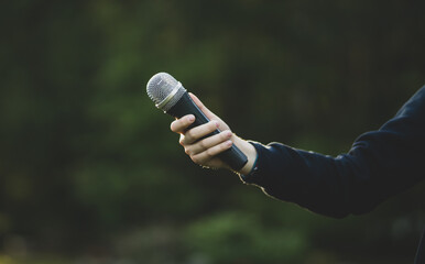A hand with a microphone on the background of nature.An open microphone.To get an...
