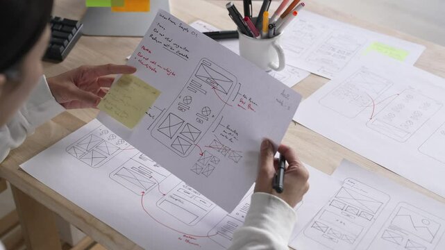 UX UI designer working on wireframes for a website and mobile app prototype, surrounded by sketches of user-flow and design tools, in concept of website and mobile application design concept.