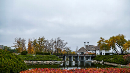 straw roofs on white houses, architecture, lake, birds in the water, yellow leaves of trees, green bushes in the autumn park, plants