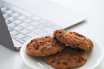 Chocolate chip cookies on a plate near a laptop. Close up.
