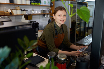 Young woman barista with mobile tablet at coffee shop counter desk