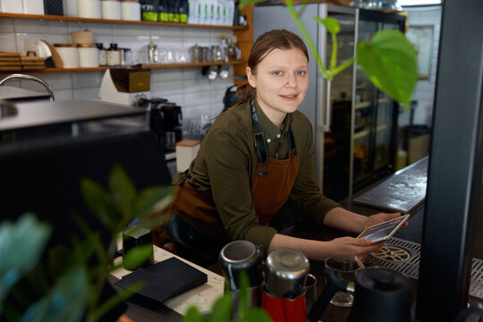 Young woman barista with mobile tablet at coffee shop counter desk