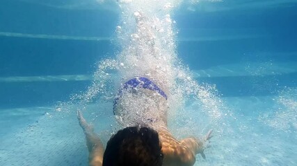 A woman gracefully swims underwater in a transparent pool. Spa and travel concept.