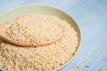 A bowl of brown rice is placed on a blue table next to a spoonful of rice.The raw rice is spread out in the bowl and the spoon is full of rice and sitting on top of it.close-up.
