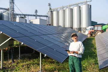 Female farmer with digital tablet on a modern farm using solar panels. Agricultural silos in the...
