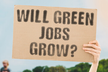 The phrase 'Will Green Jobs Grow?' on a banner in a person's hand. Human holds a cardboard with an inscription. Sustainability. Innovation. Renewable. Opportunity. Development. Economy. Future