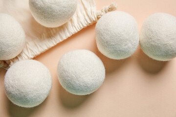 Six wool dryer balls arranged near a drawstring cotton bag on a soft beige background, top view,...