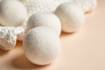 Close-up of wool dryer balls placed beside a textured white knitted fabric on a soft beige...