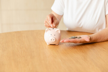 Saving money investment for future. Senior adult mature woman hands putting money coin in piggy bank. Old grandmother counting saving money planning retirement budget. Investment banking concept