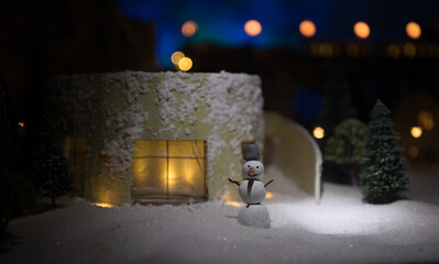 Little decorative cute small houses in snow at night in winter, Christmas and New Year miniature house in the snow at night with fir tree. Holiday concept.