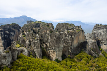 Meteroa, Greece. Majestic rock formations in rise dramatically from the landscape, offering a glimpse into nature's grandeur against the backdrop of distant snow-capped mountains