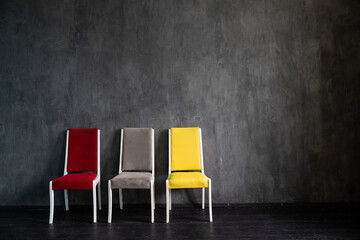 Three multicolored chairs in the interior of an empty gray room