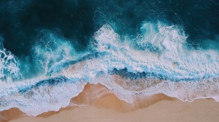 Aerial view of a sandy beach with crashing waves. The water is a deep blue and the sand is a warm beige.
