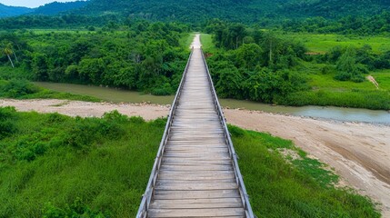 Obraz premium Scenic Wooden Bridge Over Waterway Surrounded by Lush Green Landscape and Mountains in the Background, Ideal for Nature and Adventure Themes