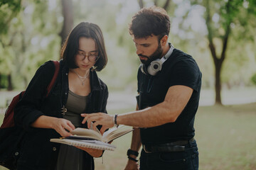 Two students engage with a professor in a park, reviewing study materials together after classes in...