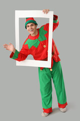 Obraz premium Handsome young man in elf's costume with frame waving hand on grey background