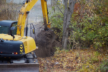 An excavator bucket filled with soil spilling onto the ground, excavator work in the autumn season,...