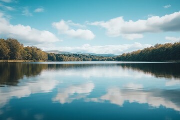 Fototapeta premium A serene lake landscape reflects the beauty of nature. Soft clouds float in the blue sky above the calm water. This tranquil scene invites relaxation and peace. Generative AI