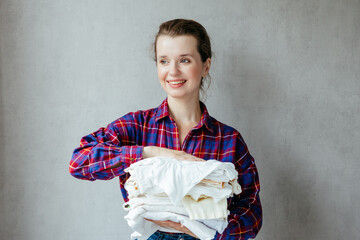 happy woman holds stack of clean white clothes in hands after washing, drying. Feel softness of your clothes after dry cleaning. young laundress in household is doing housework. close-up, portrait.
