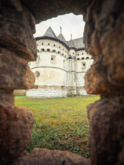 portrait view through hole in stone fence to old defence fortress-church in Ukraine in autumn day