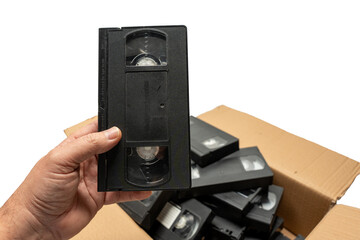 Obraz premium A person is holding a black VHS tape in a box full of other black VHS tapes. The box is filled with various tapes, some of which are in different sizes and shapes