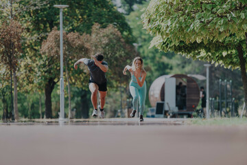 Energetic friends sprint side by side on a sunny day in a beautiful park. The vibrant atmosphere highlights their dedication to fitness and outdoor exercise.