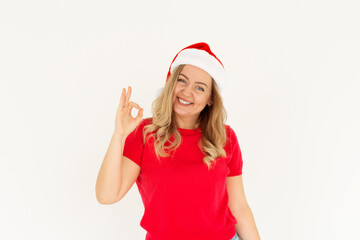Young funny european woman in red t-shirt and christmas hat showing ok sign and smiling. Happy New Year and Merry Christmas concept