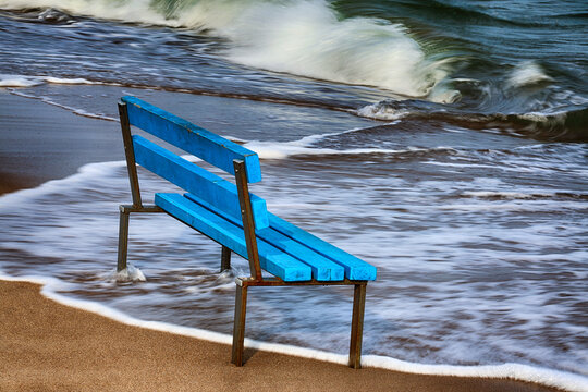 Niebieska ławka na ż&oacute;łtej plaży nad morzem. 
