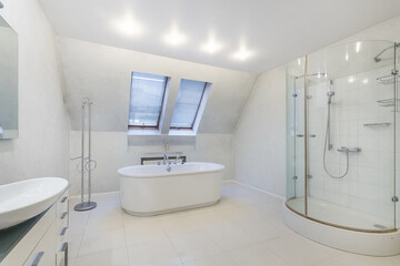 A modern bright bathroom with windows over the bathtub and an oval glass shower cabin.