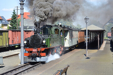 A smoking steam locomotive carrying passengers stands at the station.