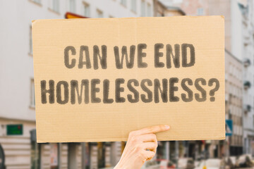 The phrase 'Can We End Homelessness?' on a banner in a person's hand. Human holds a cardboard with an inscription. Compassion. Dignity. Shelter. Support. Community. Change. Hope