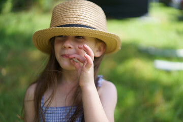 Cute little girl in a sundress and a straw hat on a lawn on a farm background close-up. Concept of children's health, rest, travel, fun and well-being
