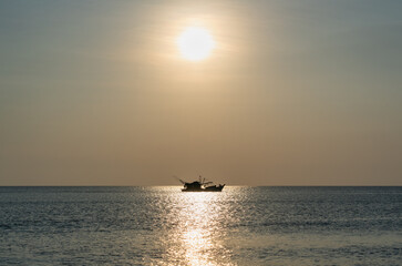 A solitary fishing boat at sunset with a bright sun over the calm sea, creating a serene and peaceful atmosphere