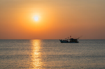 A solitary fishing boat at sunset with a bright sun over the calm sea, creating a serene and peaceful atmosphere